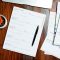 a wooden table topped with papers and a pen excel spreadsheet, rent tracker, landlord tools