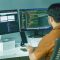 a man sitting in front of two computer monitors farmer in office, farm management software dashboard, financial charts on screen
