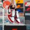 Hand holding red and white nike sneakers over box. sneaker authentication process, sneaker inspection table, sneaker quality control, shoe expert examining shoes